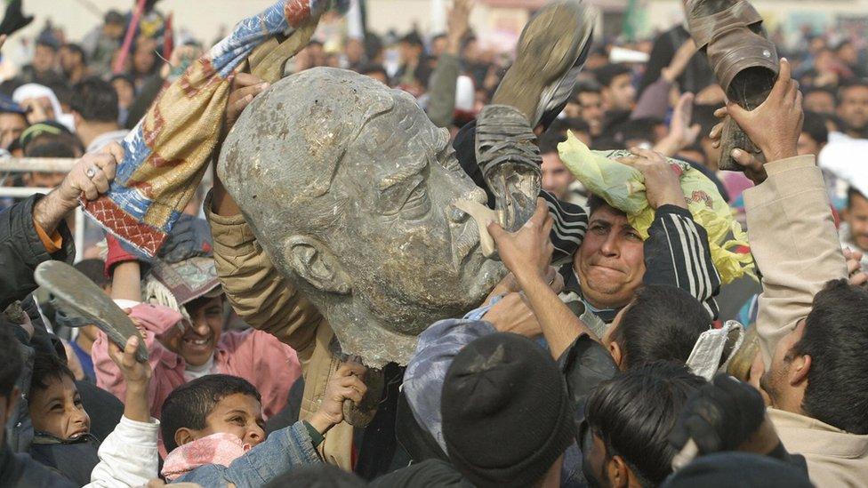 Iraqis with part of the statue of former dictator Saddam Hussein