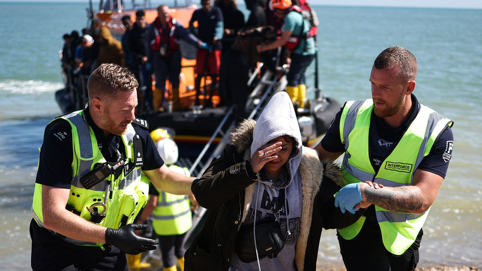 An interforce officer and a border force officer help a woman on the beach at Dungeness on the southeast coast of England, on 16 August 2023