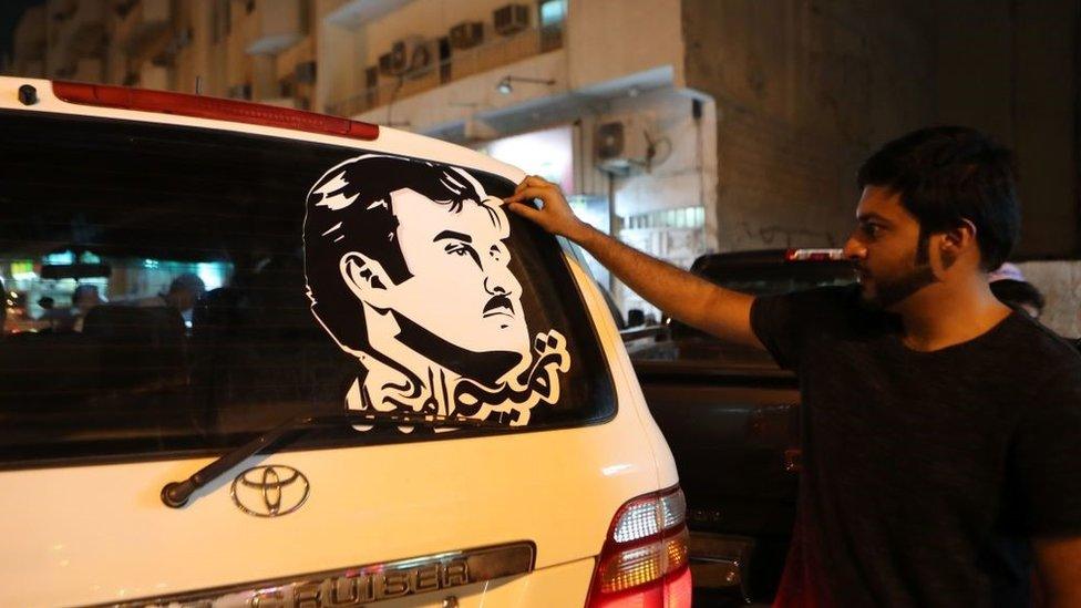 Doha man puts on a car a sticker portraying Qatar's Emir Sheikh Tamim bin Hamad Al-Thani