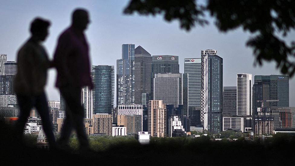 People walk in front of Canary Wharf buildings in the background