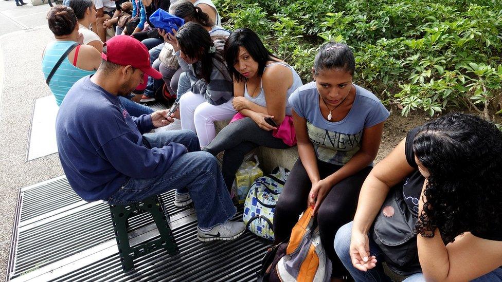 people queue to try to buy groceries and goods outside a supermarket in Caracas on 11 November