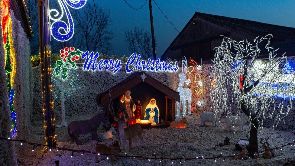 An illuminated nativity scene, Merry Christmas sign and light-covered trees.