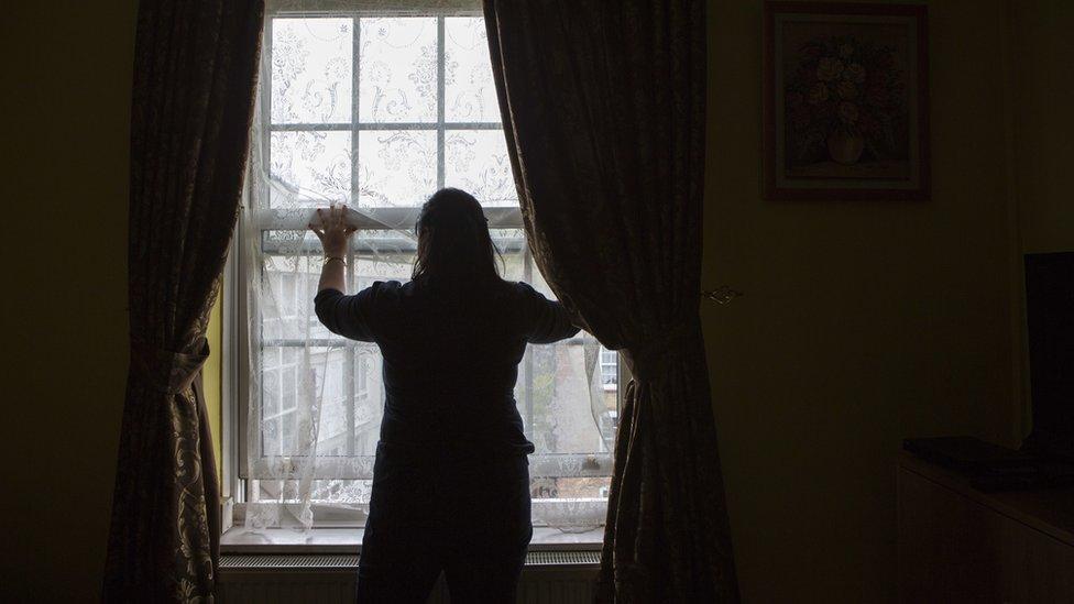 An unidentified lady stands silhouetted in front of her living room window