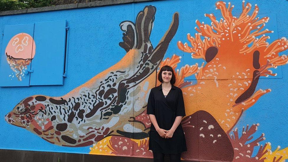 Artist Georgia Green standing in front of her mural showing a seal and sea anemonies