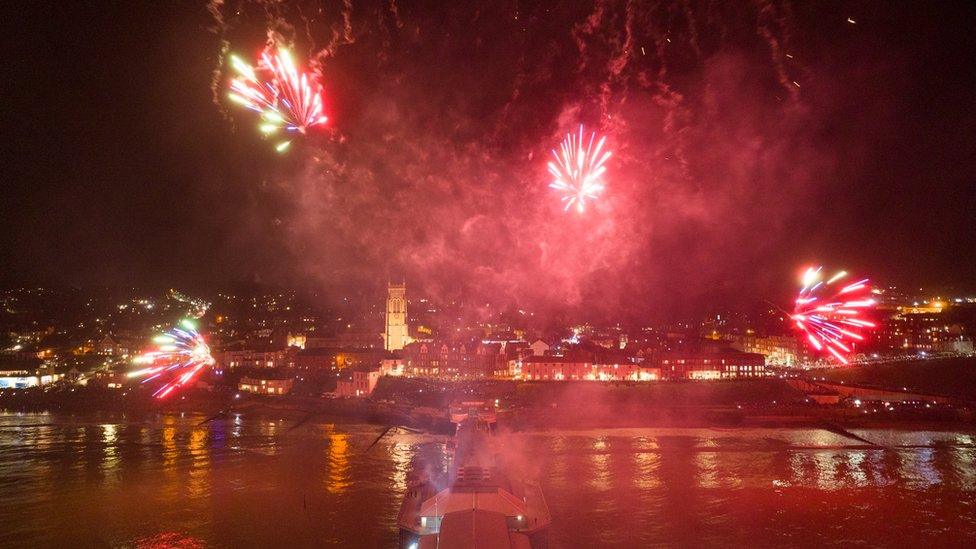 Red fireworks reflect off the water by Cromer Pier