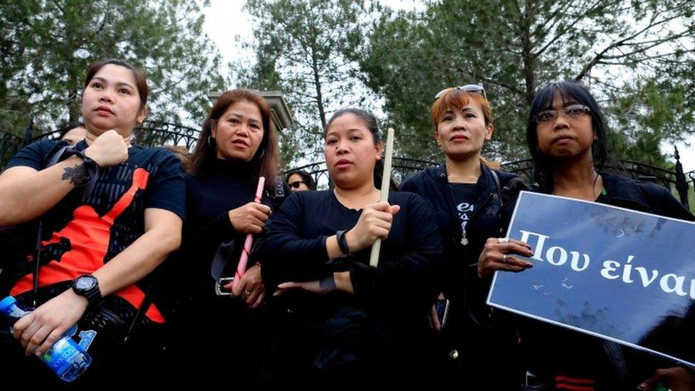 Five female migrant workers in Cyprus stand in solidarity, holding a banner that reads "Where are you?"