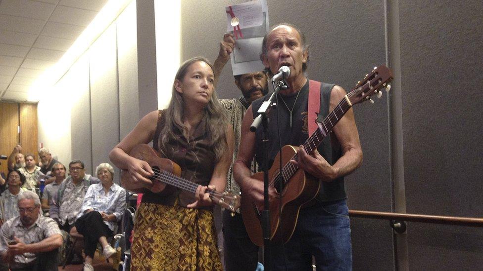 Laulani Teale, left, and Liko Martin, right, sing while Palani Vaughan, centre rear, holds up a copy of Queen Liliuokalani's protest of the overthrow of Hawaii at the Hawaii state Capitol in Honolulu on Monday, June 23, 2014.