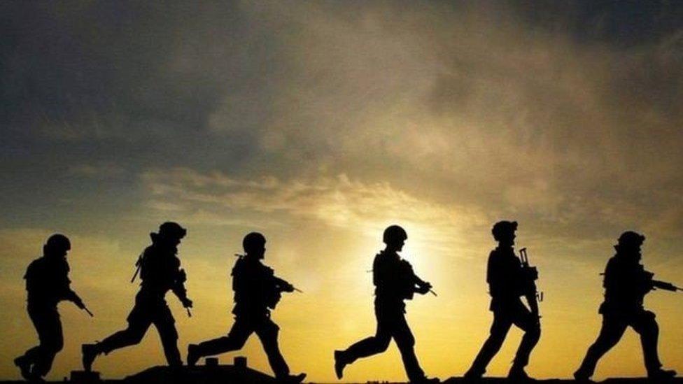 A photograph of silhouettes of soldiers walking against a sky backdrop