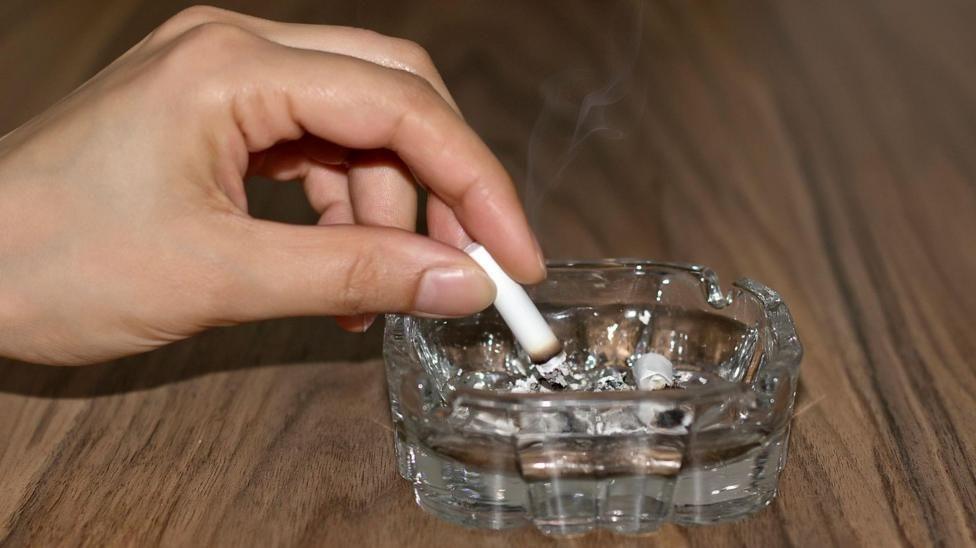 A hand stubbing out a cigarette in a glass ashtray.