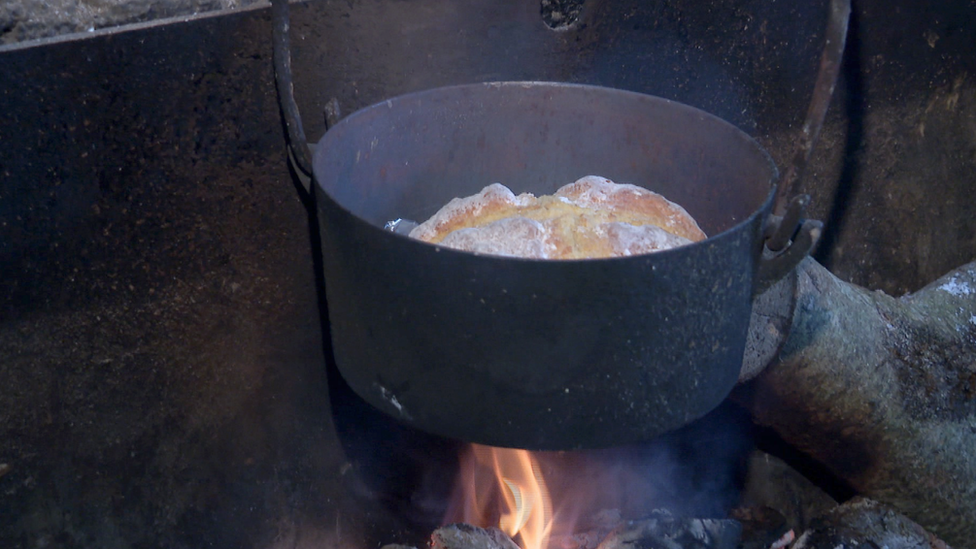 A pot of soda bread cooking over an open fire