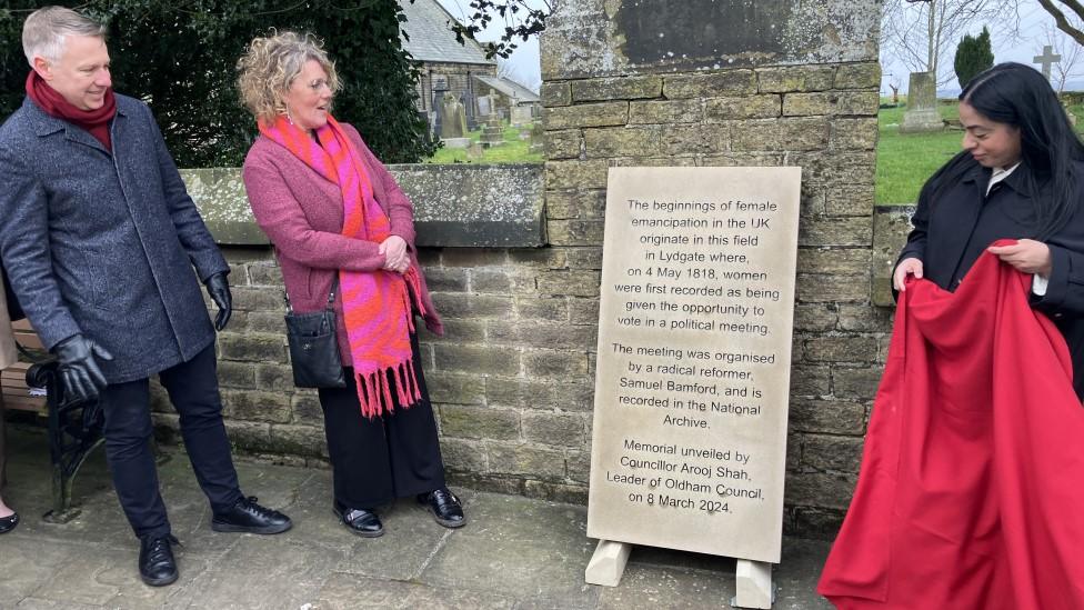 Three people looking at a large plaque