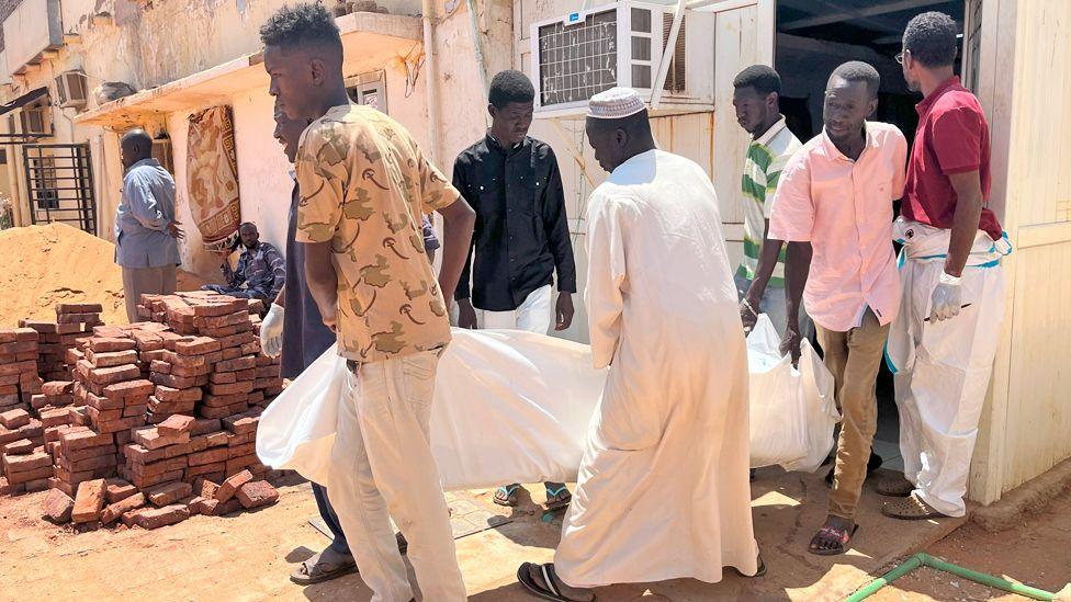 Five men outside a morgue in Omdurman carry a body in a white sheet 