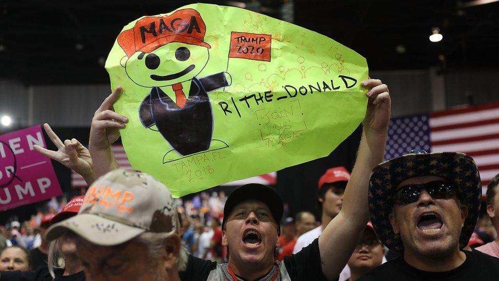 Picture of a man holding up a sign referencing the subreddit board "The Donald". The QAnon conspiracy has spread to mainstream social networks such as Reddit