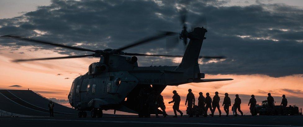 The silhouette of Royal Marines with a helicopter