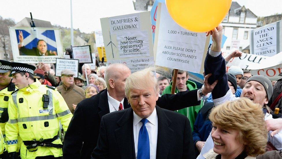 A protester rubs Donald Trump's hair with a balloon, making it stand up