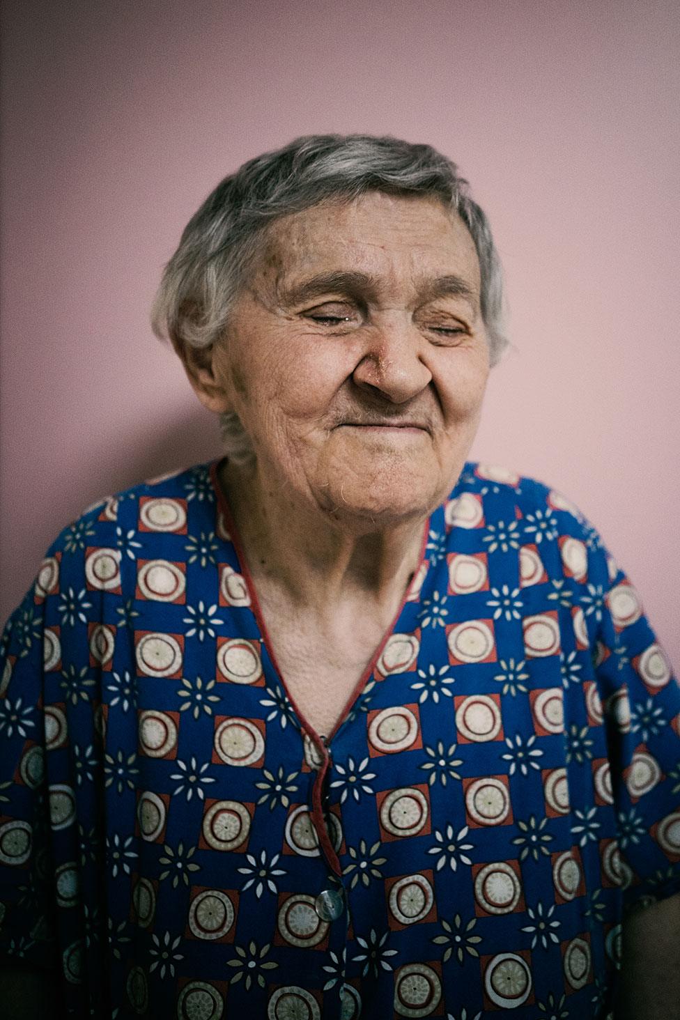 A blind woman poses for a portrait against a pink wall