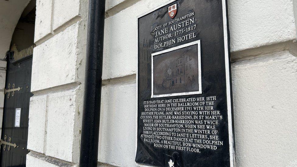 Black plaque with white writing and artwork detailing the hotels links with Jane Austen