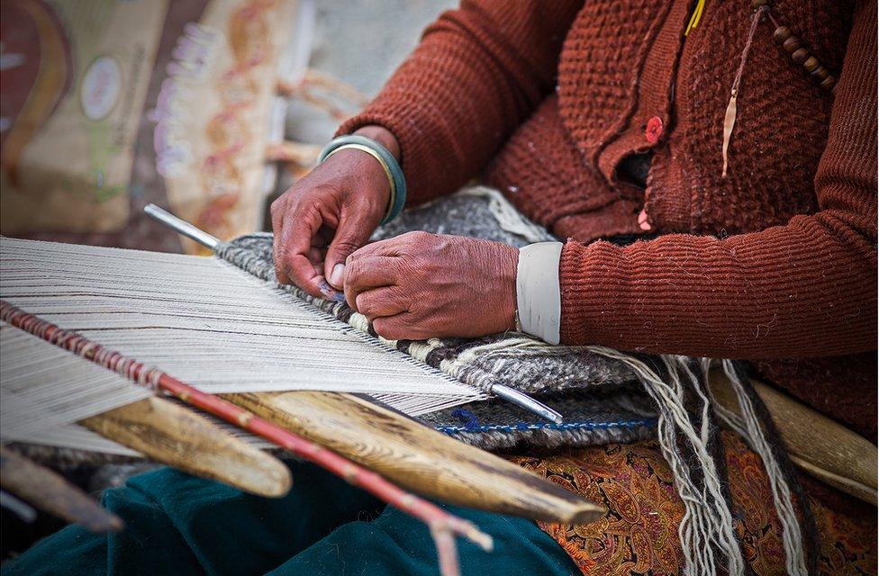 A woman weaves threads on a loom on her lap