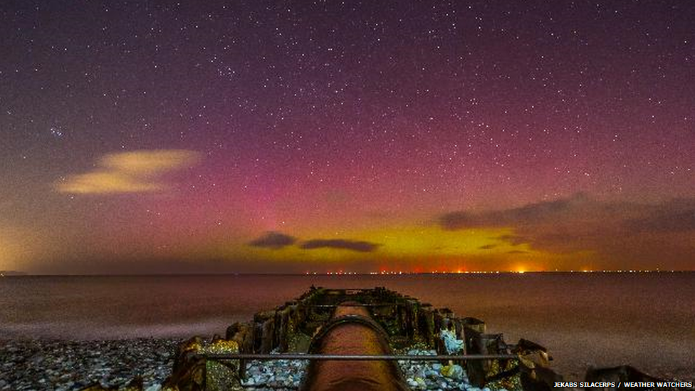 Green and purple tinges in the night sky with a jetty in the foreground.