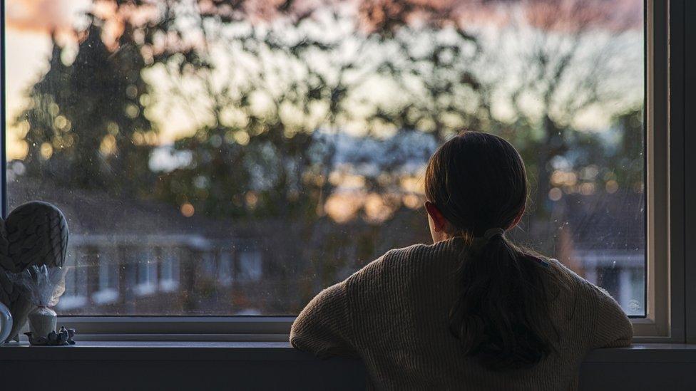 Child staring out the window at sunset