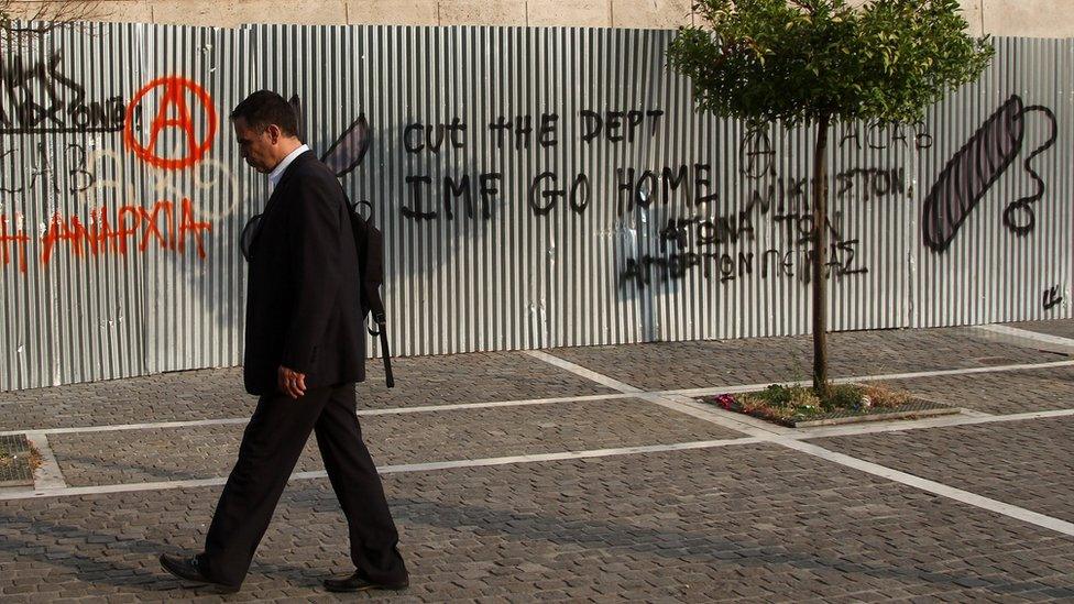 Man walks past wall with graffiti reading "IMF go home"