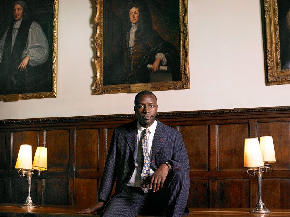 Portrait of British writer Diran Adebayo standing in front of paintings on the wall