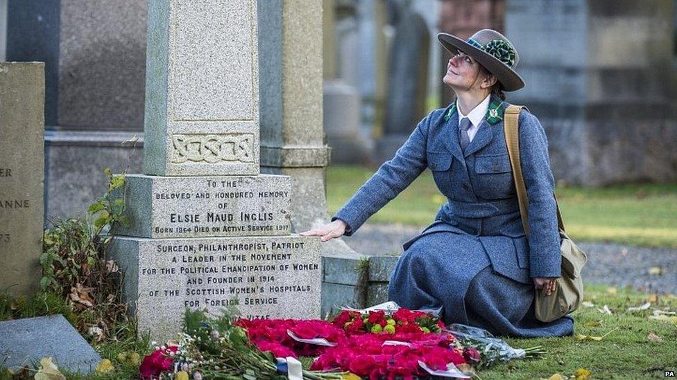 A woman wearing the uniform of Scottish Women's Hospitals kneels by the grave of Dr Elsie Inglis