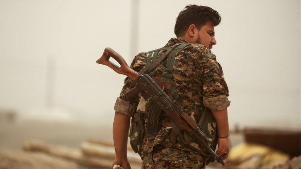 A member of the Kurdish People's Protection Units (YPG) walks with a Kalashnikov assault rifle slung behind his back in the town of al-Karamah, 26km from Raqqa, on 10 May 2017