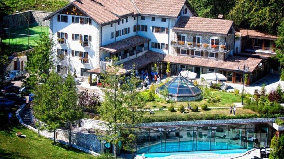 The hotel in summer - a white, L-shaped four-storey building with green gardens