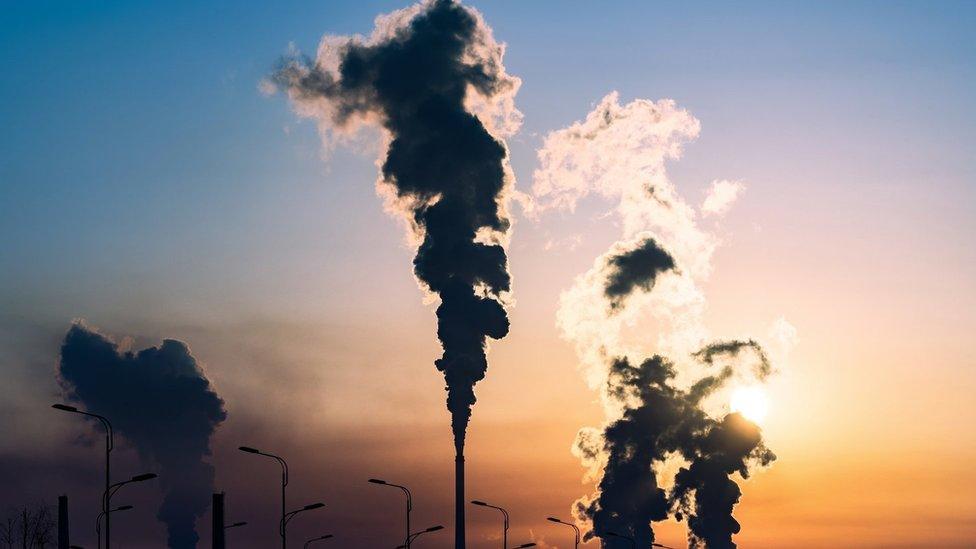 chimneys billowing smoke in front of a setting sun