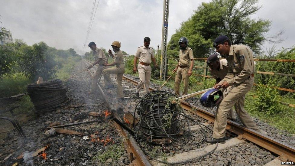 Policemen remove cables from a railway track which were set on fire by the protesters in Ahmedabad, India, August 26, 2015.