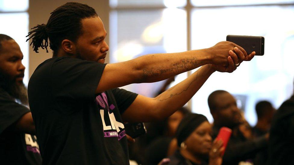 An attendee of the special council meeting holds a phone like a gun