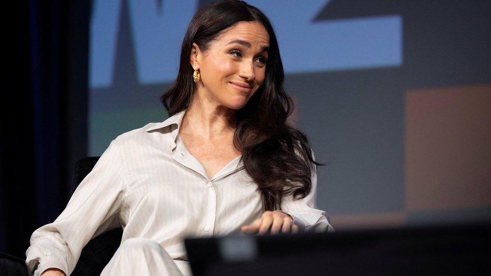 Meghan in silky white shirt, looking over