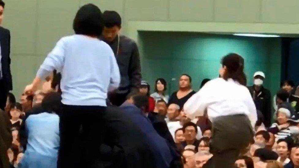 A photo grab from a Youtube video shows women climbing up a sumo ring to treat Maizuru city mayor Ryozo Tatami, who collapsed while making a speech in a gym in Maizuru, Kyoto prefecture, Japan April 4,