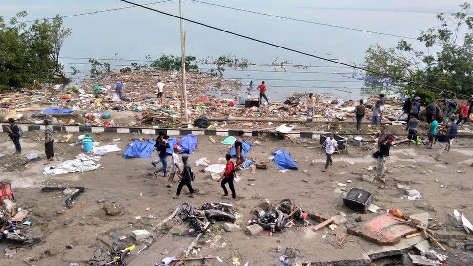 People walk past dead bodies (blue cover) in Palu. Photo: 29 September 2018