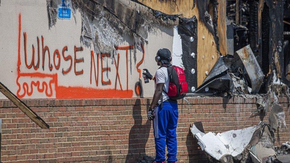 A man spray paints a message onto the wall of a restaurant destroyed after the Atlanta police shooting on 12 June