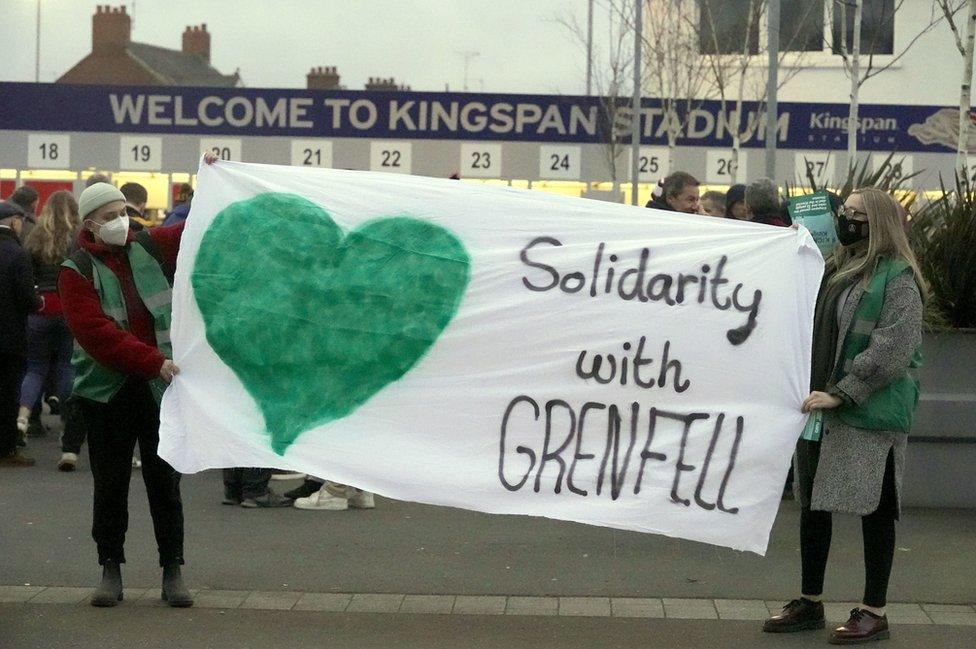 People standing outside Ulster Rugby's Kingspan Stadium, holding a banner that reads: Solidarity with Grenfell