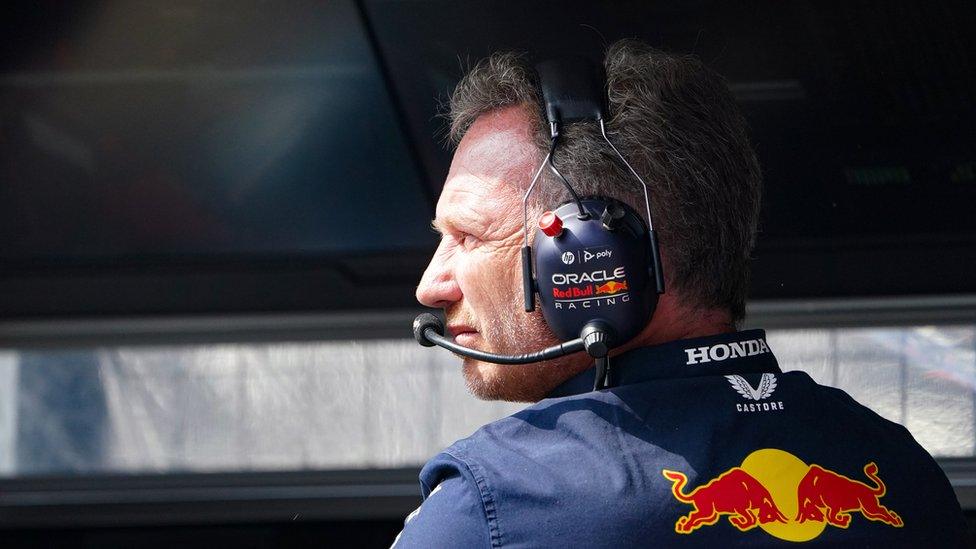 Man with short dark hair wearing Red Bull clothing and a headset watches an F1 race