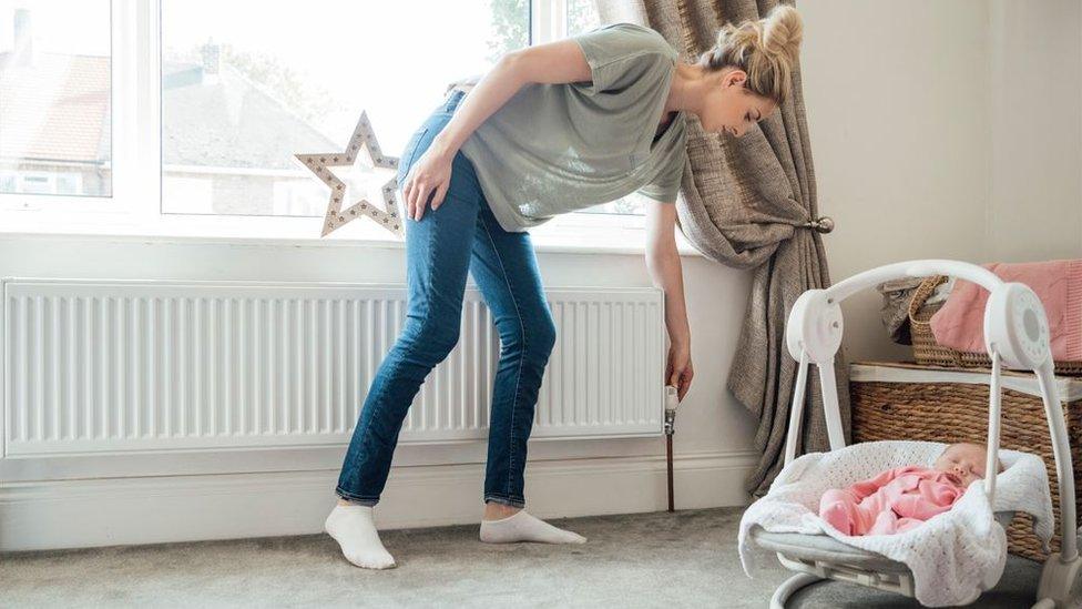 Woman with baby adjusting thermostat on radiator