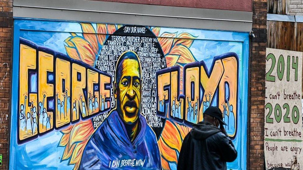 A man walks past the mural of George Floyd