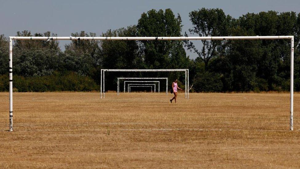 A woman walks across the brown grass of parched football pitches on Hackney Marshes, east London