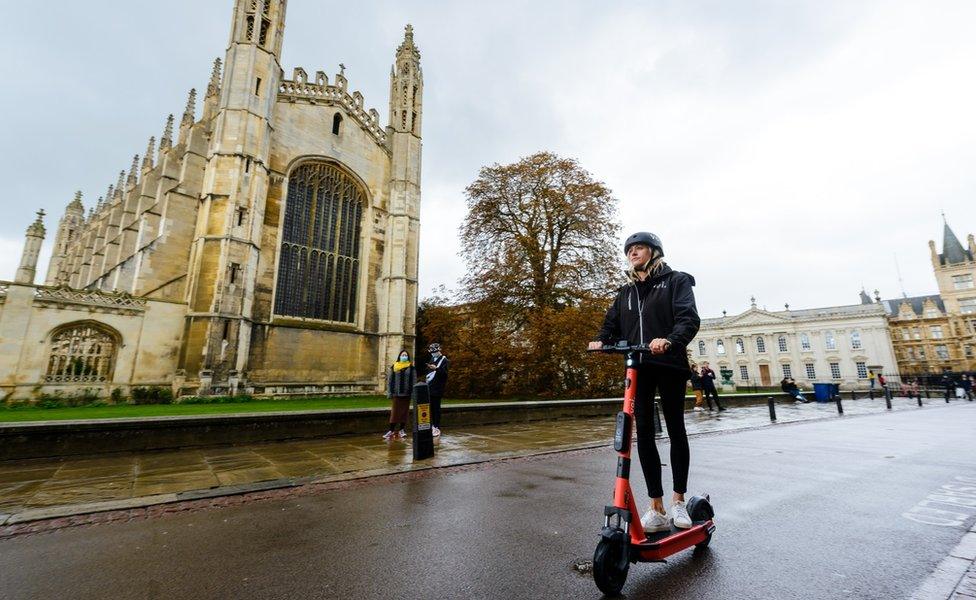 Woman riding past King's College Chapel in Cambridge on e-scooter