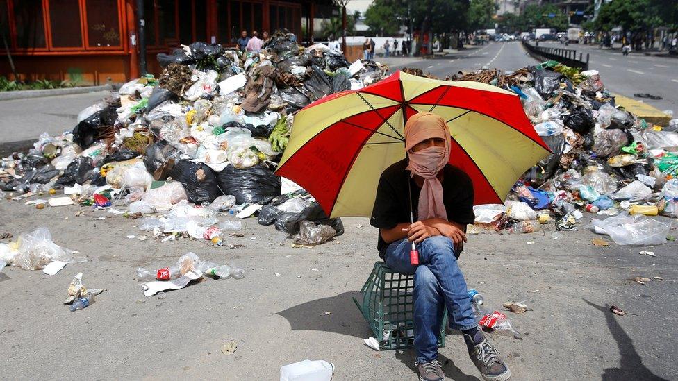 A demonstrator sits under an umbrella next to a pile of rubbish used as barricade in Caracas, Venezuela June 29, 2017