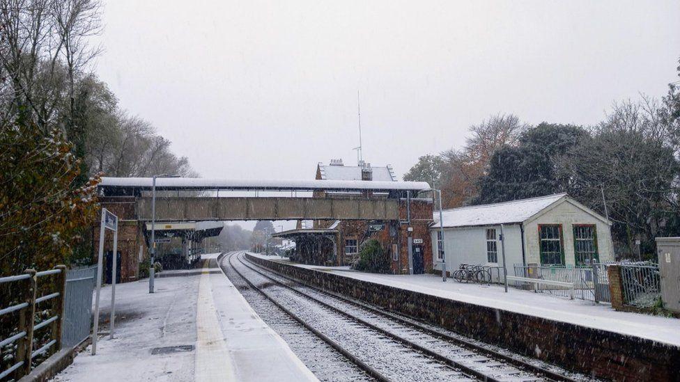 Snow covered train tracks running through railway station with buidings either side.