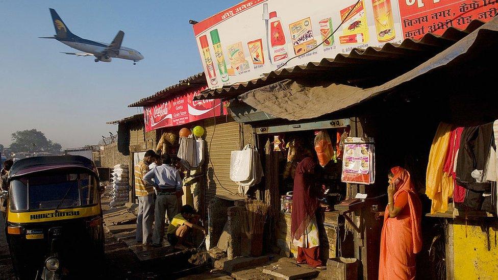 A woman talks on her cell phone as a passenger jet flies over the Jari Mari slum before landing at Mumbai Airport, on February 3, 2009 in Mumbai, India.