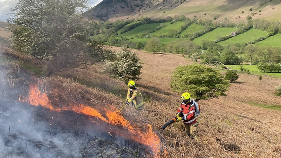 Two firefighters hosing down a grass fire in a field in Talgarth