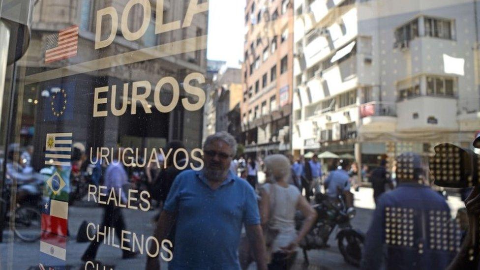 People reflects on the window of a closed bureau de change in downtown Buenos Aires on December 16, 2015. Argentina said Wednesday it will eliminate the foreign exchange restrictions that have propped up the official value of the peso since 2011, setting up a potentially painful devaluation. AFP