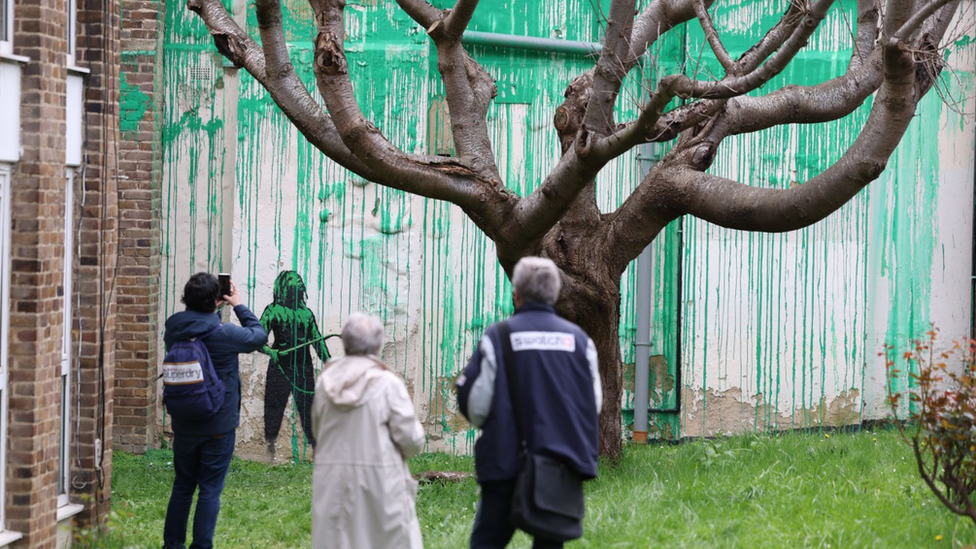 People view a graffitied mural near a tree on Hornsey Road in the Finsbury Park area of London