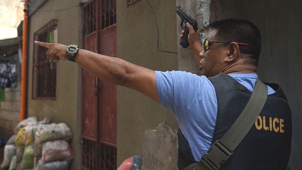 A plainclothes policeman takes position as police serve a search warrant to a resident in relation to drugs at an informal settler house in Pasig City