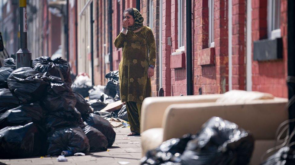 Woman covers her mouth amid bin bags